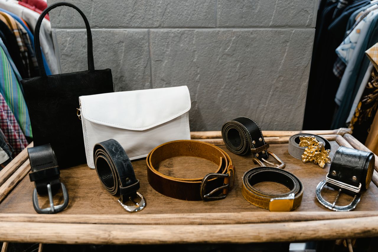 Home A collection of stylish belts and handbags displayed on a wooden rack in a fashion boutique.
